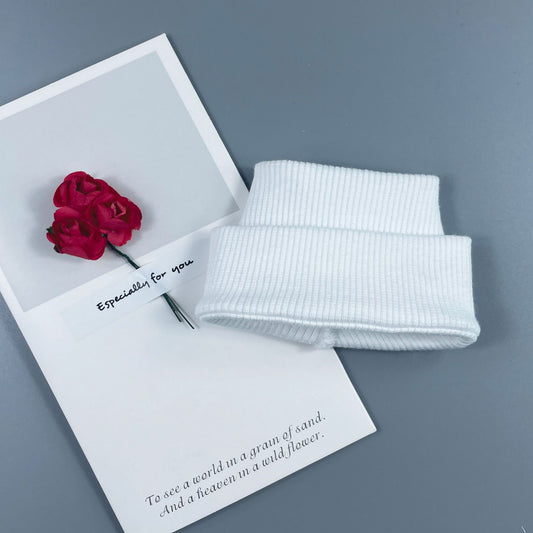White ribbed knitted headband with a red rose on a gray background