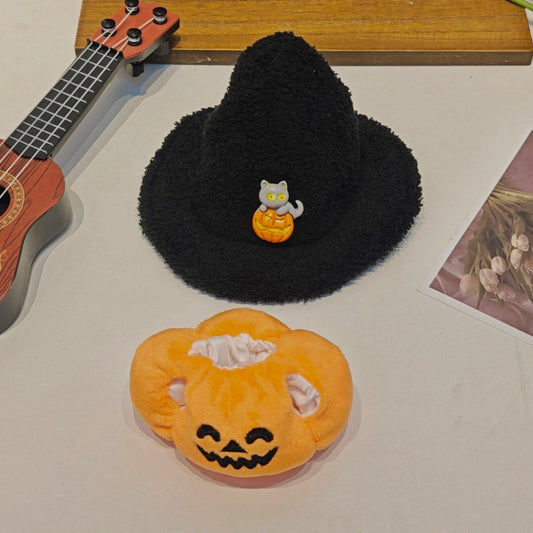 Black witch hat with a cat on a pumpkin and orange shoes with a pumpkin design on a light surface.