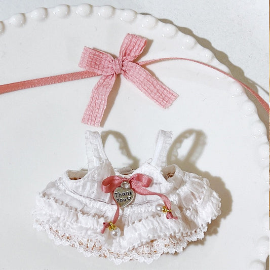 White lace baby dress with pink ribbon and 'Thank You' heart charm on a white plate.