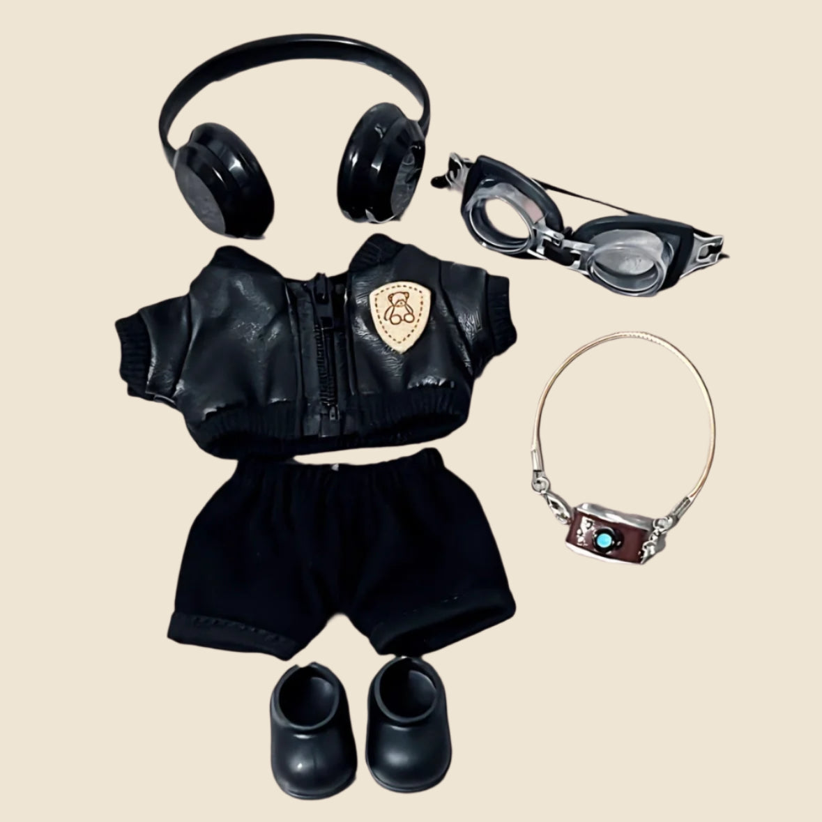 Black outfit with jacket, shorts, shoes, headphones, goggles, and bracelet on a beige background